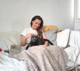 Fanny, assise sur un canapé, caresse une chatte écaille de tortue posée sur une couverture.